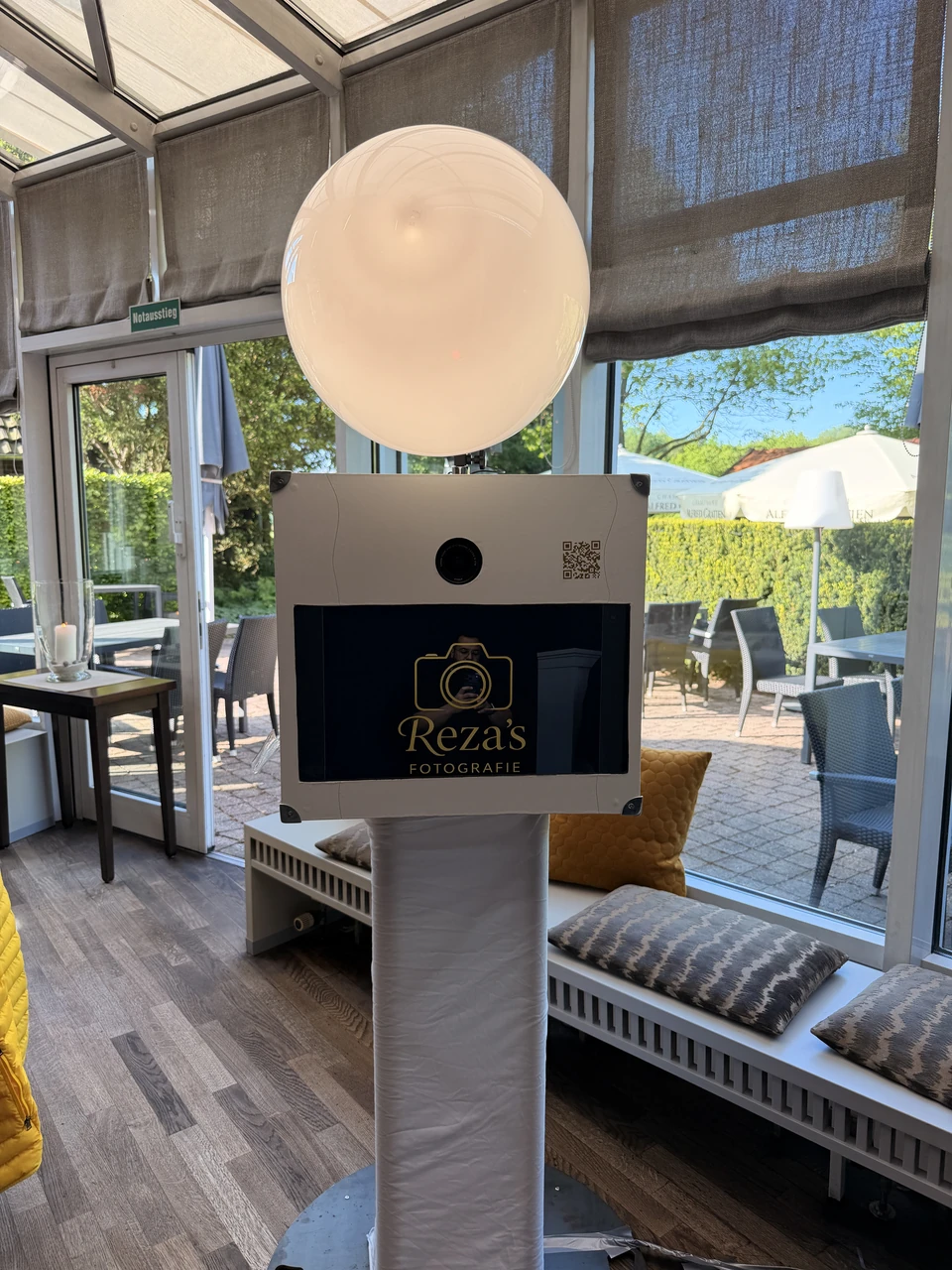 Rezas weiße Fotobox mit rundem Blitz und eigenem Logo auf dem Bildschirm